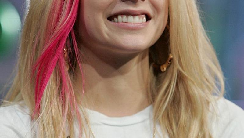 Avril Lavigne într-un tricou alb, are părul blond și o șuviță roz