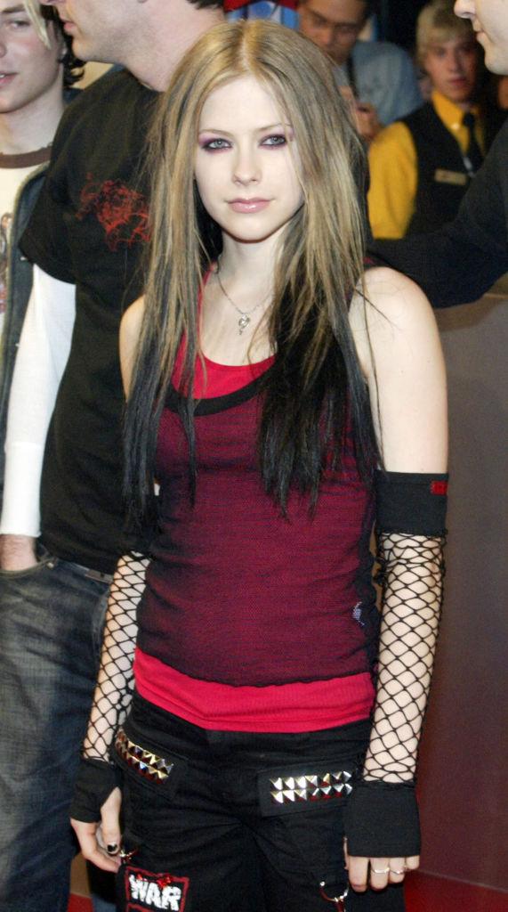 Avril Lavigne intr-o ținută neagră cu plasă, iar părul îl are jumătate șaten, jumătate brunet