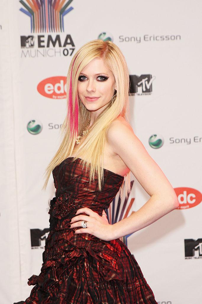 Avril Lavigne pe covorul rosu, intr-o rochie fara bretele, visinie și parul blond cu suvite