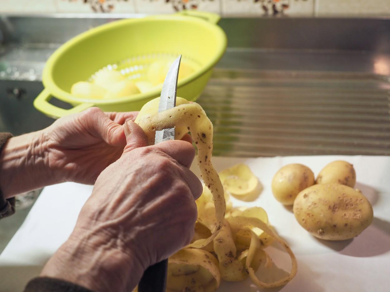 imagine ilustrativă cu mâinile unei persoane care curăță cartofi