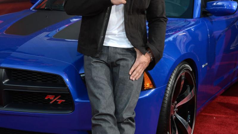 Vin Diesel într-o geacă neagră și tricou alb, stă pe mașină