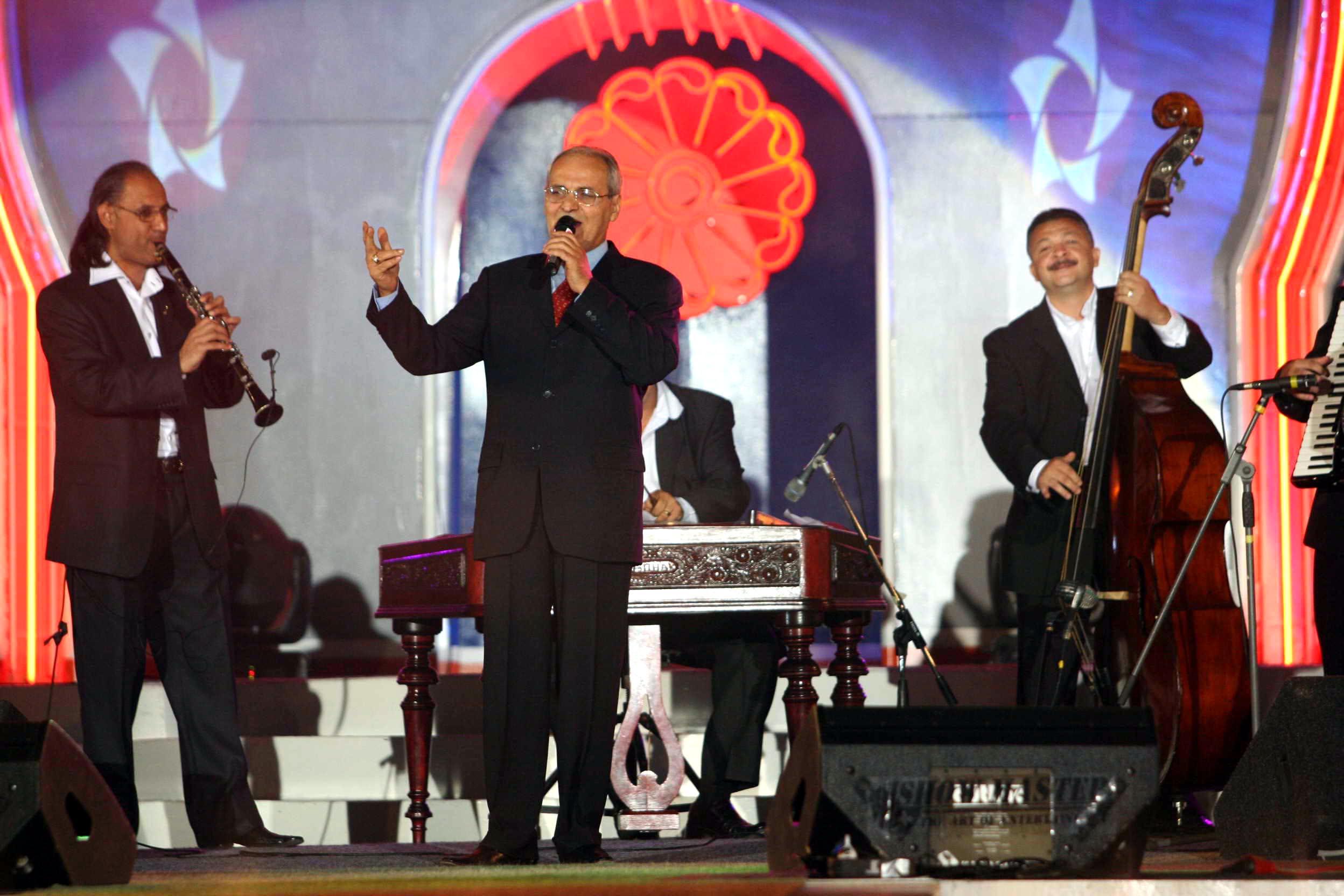 Nelu Ploieșteanu într-un costum negru, pe scenă, cântă la microfon