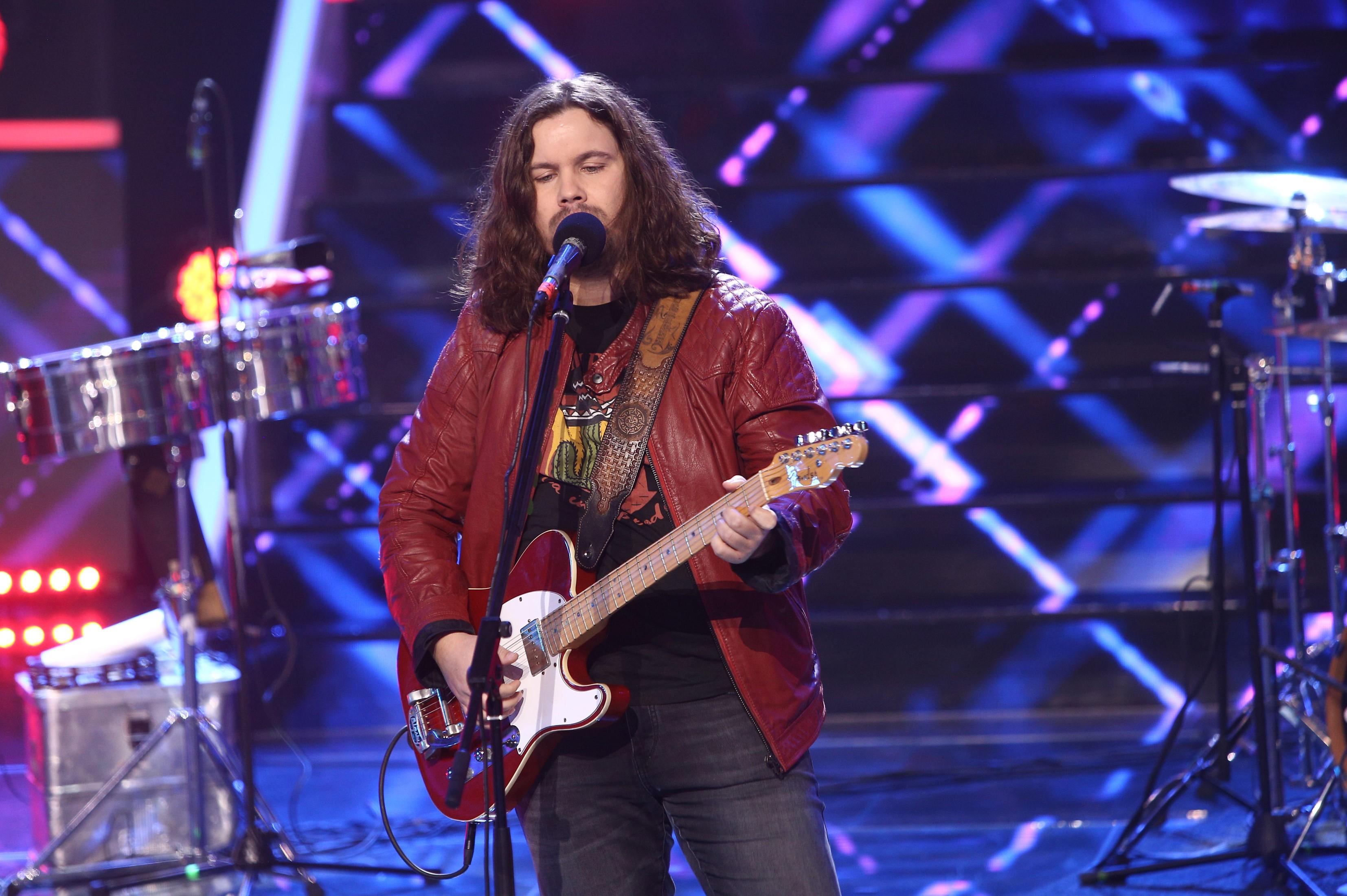 Radu Almășan într-o geacă roșie, cântă la chitară