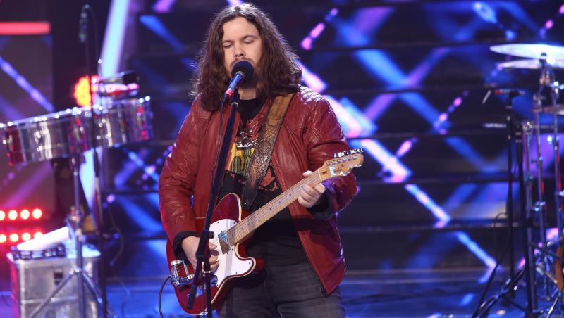 Radu Almășan într-o geacă roșie, cântă la chitară