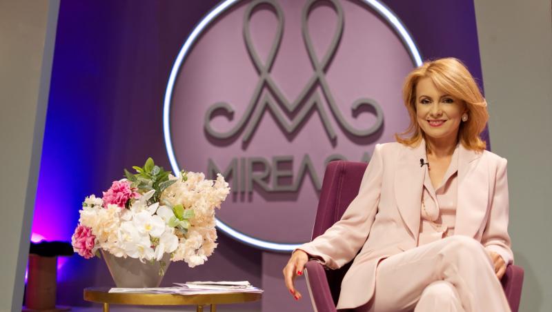 Simona Gherghe, într-un costum alb, stând pe scaun, în platoul emisiunii Mireasa