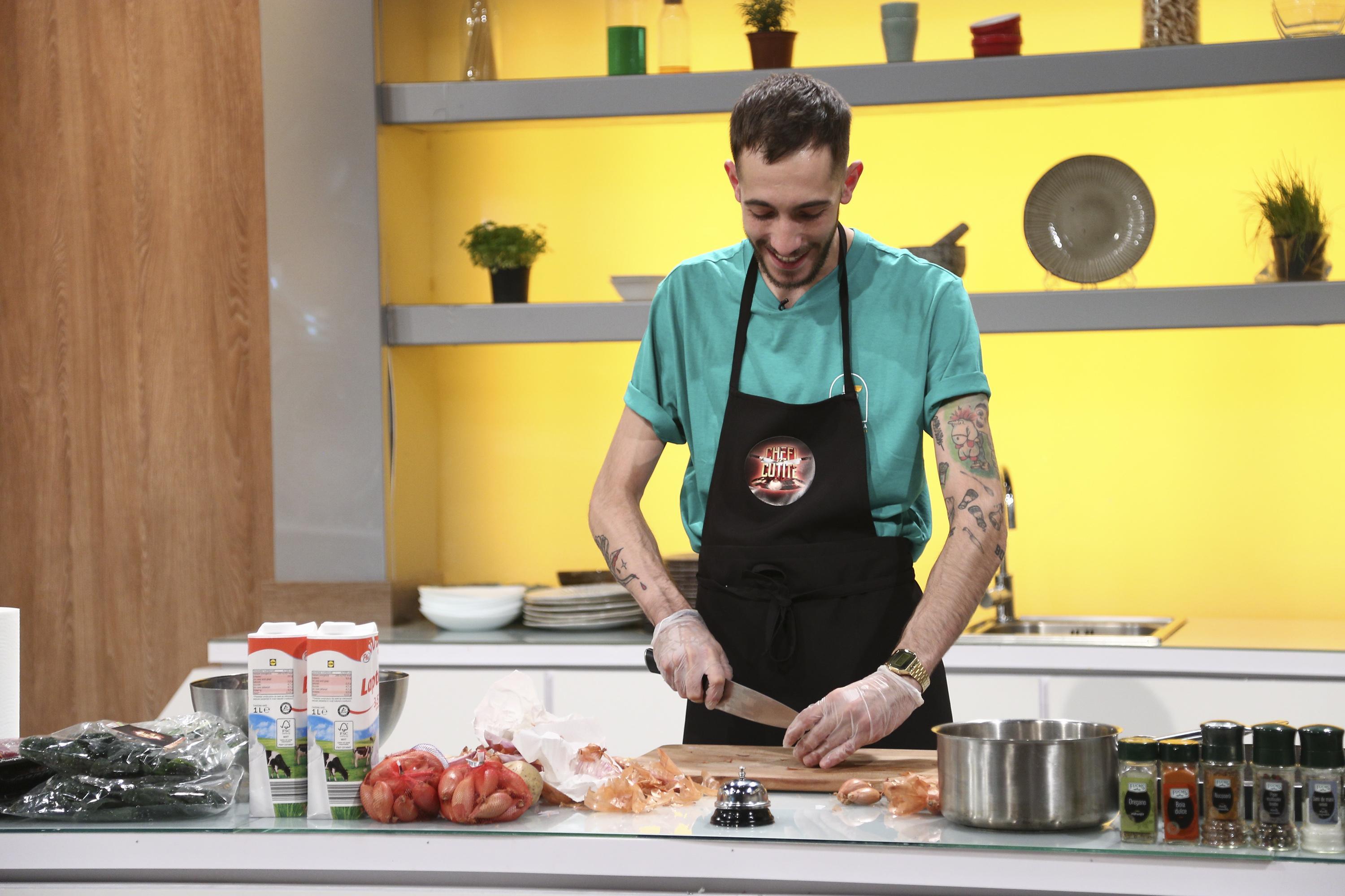 Luca Pintea, îmbrăcat în tricou verde și șorț negru, cu emblema Chefi la cuțite, taie câteva roșii la masa de gătit