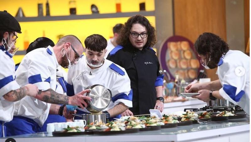 Theo Costache, îmbrăcat în tunică alb albastră, gătește alături de un alt coleg de echipă. În spatele lor este Chef Florin Dumitrescu, care urmărește ce fac cei doi