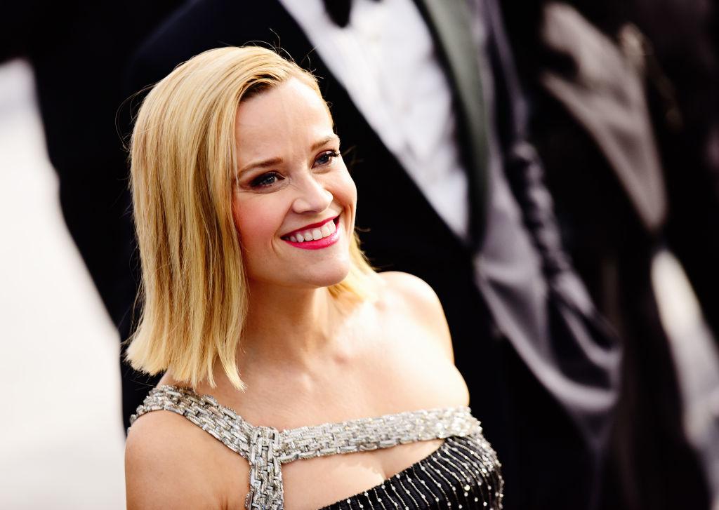 Reese Witherspoon îmbrăcată într-o rochie, cu părul desfăcut, râde