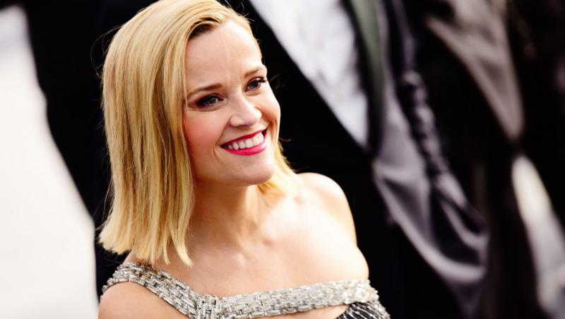 Reese Witherspoon îmbrăcată într-o rochie, cu părul desfăcut, râde
