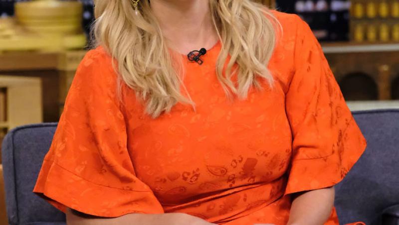 Reese Witherspoon îmbrăcată într-o rochie portocalie, cu părul desfăcut, râde