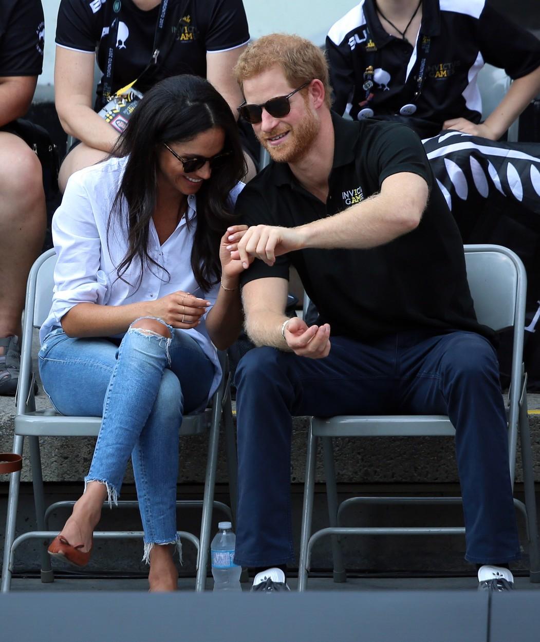 Prințul Harry și Meghan Markle stau pe scaune, unul lângă altul, îmbrăcați casual