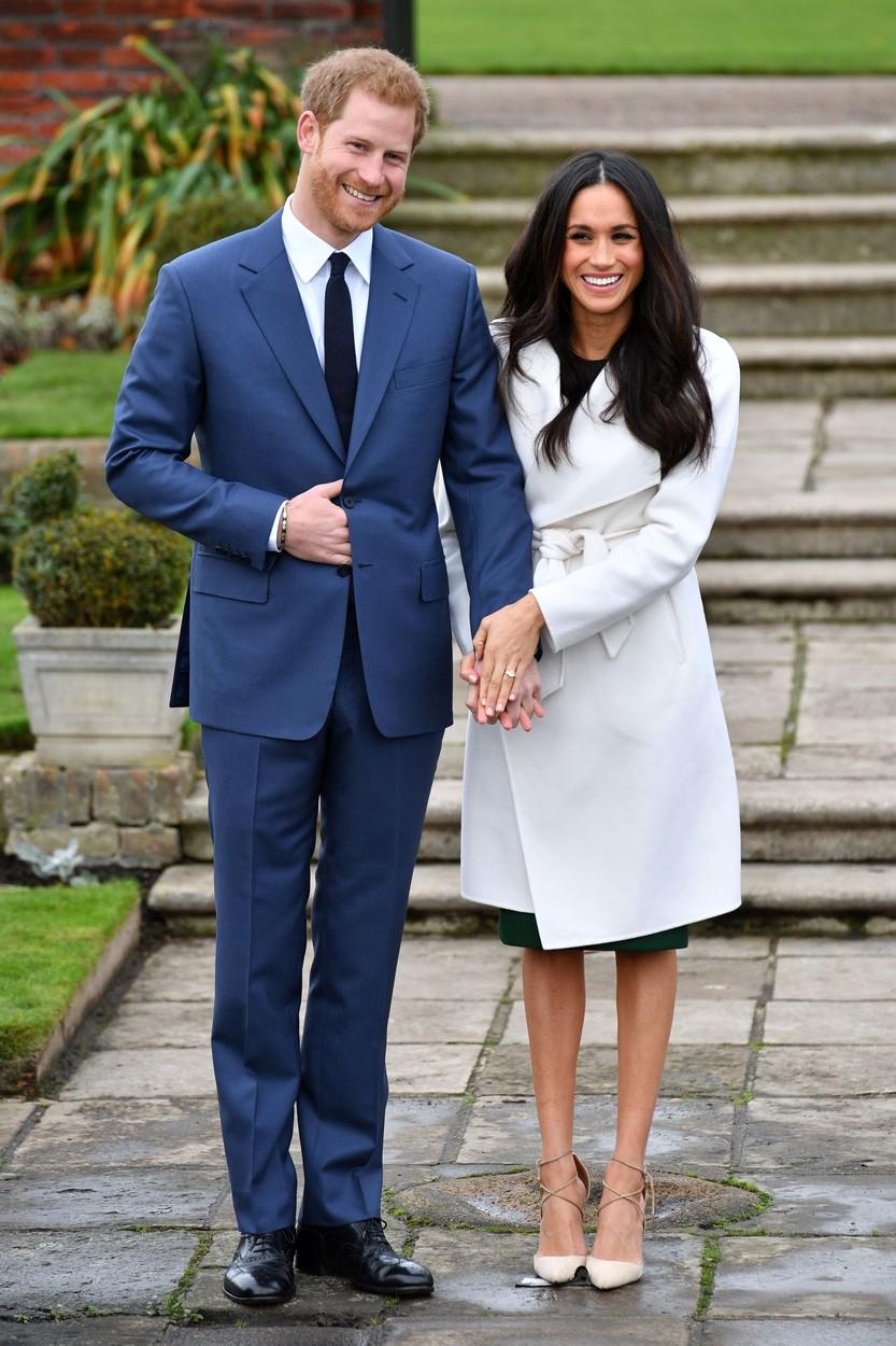 Prințul Harry și Meghan Markle, îmbrăcați elegant. El este într-un costum albastru, ea în rochie și palton deschis la culoare