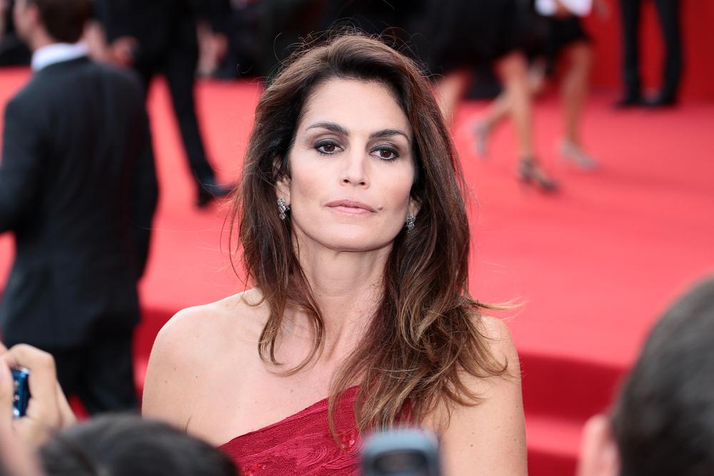 Cindy Crawford, cu părul desfăcut, îmbrăcată într-o rochie roșie, pe un umăr