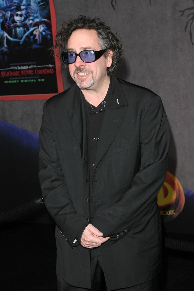 Tim Burton poartă ochelari la ochi, îmbrăcat în costum negru și cămașă neagră