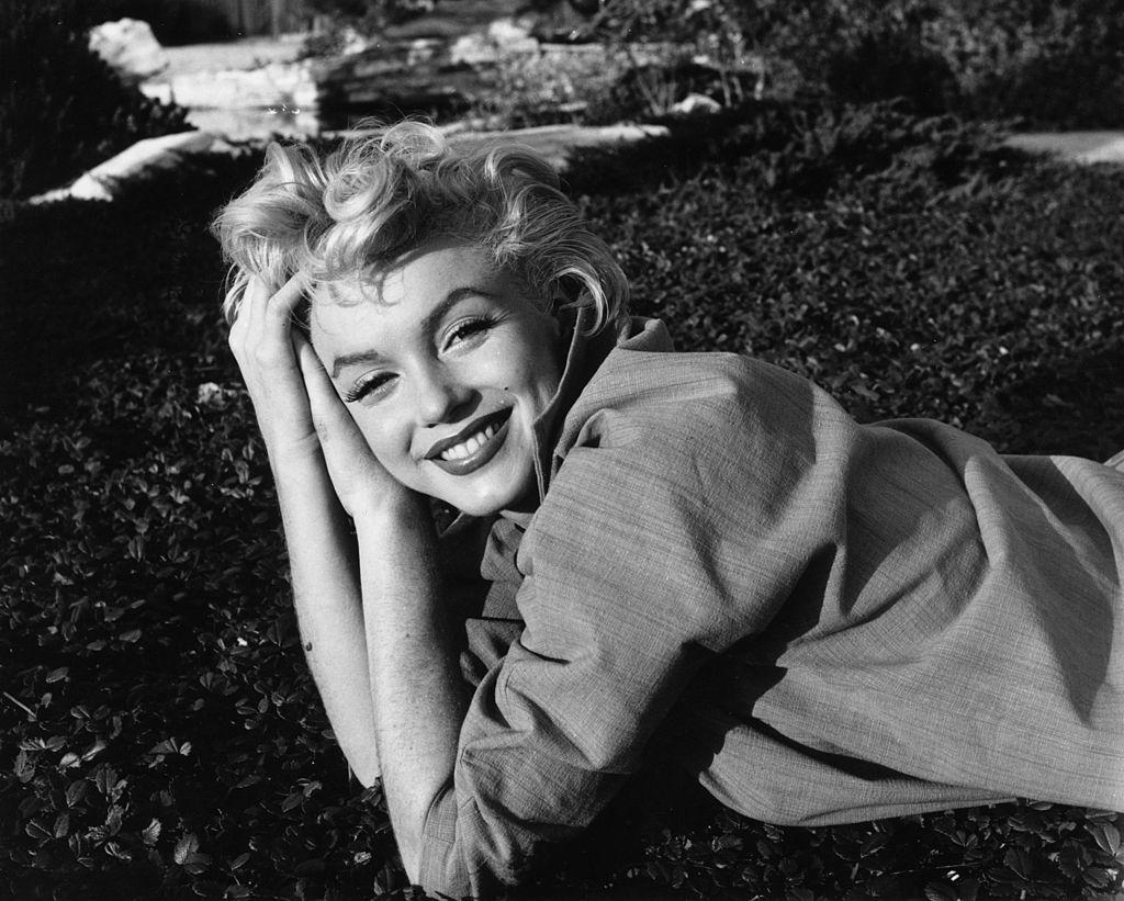 Marilyn Monroe, zâmbitoare, întinsă pe jos, fotografie alb negru