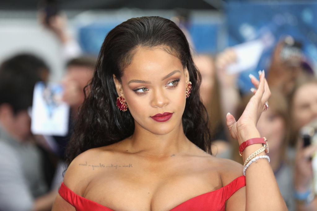 Rihanna, cu părul lung, desfăcut, îmbrăcată într-o rochie roșie, căzută pe umeri