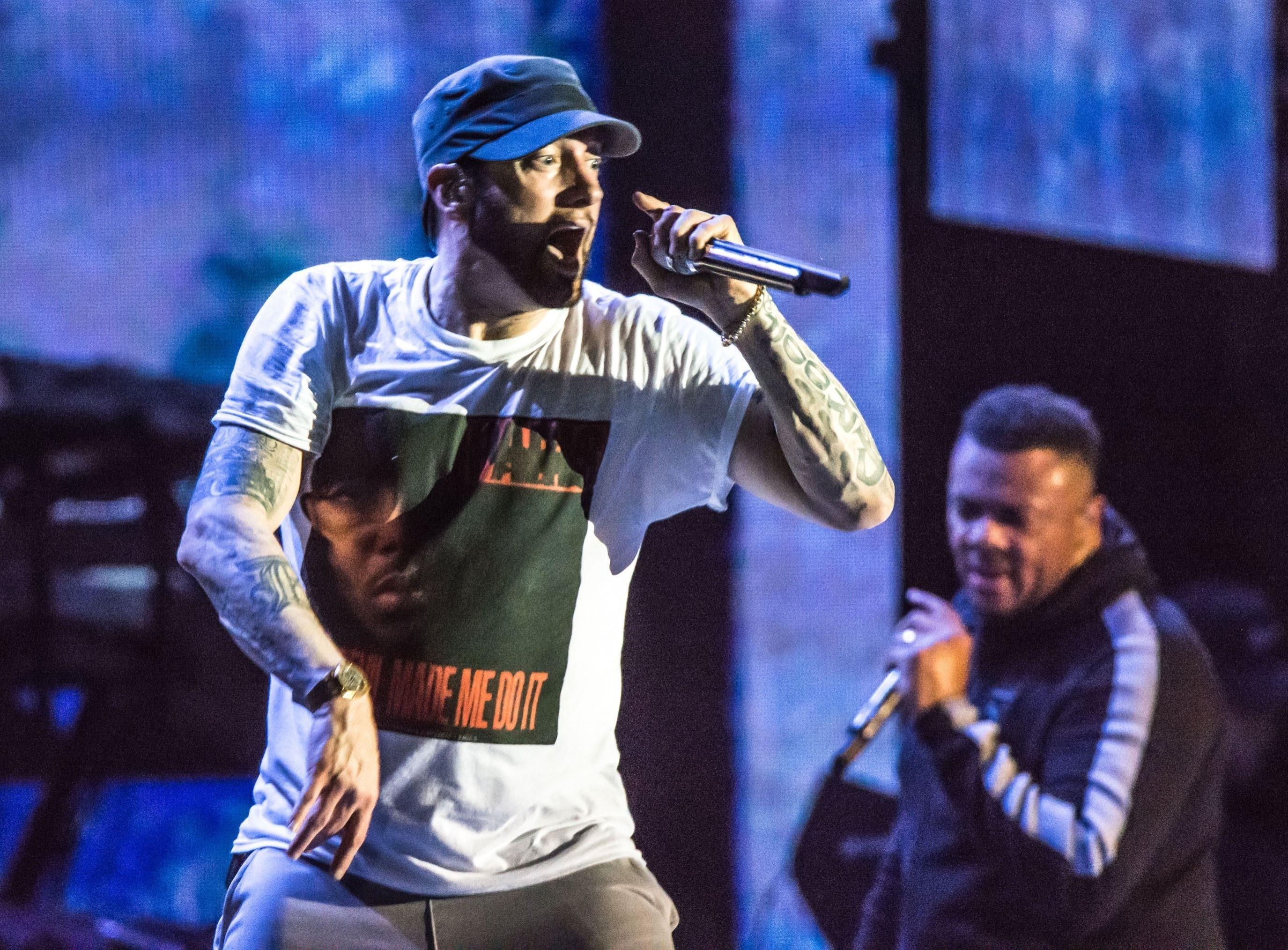 Eminem, îmbrăcat cu un tricou alb, cântă pe scenă, live
