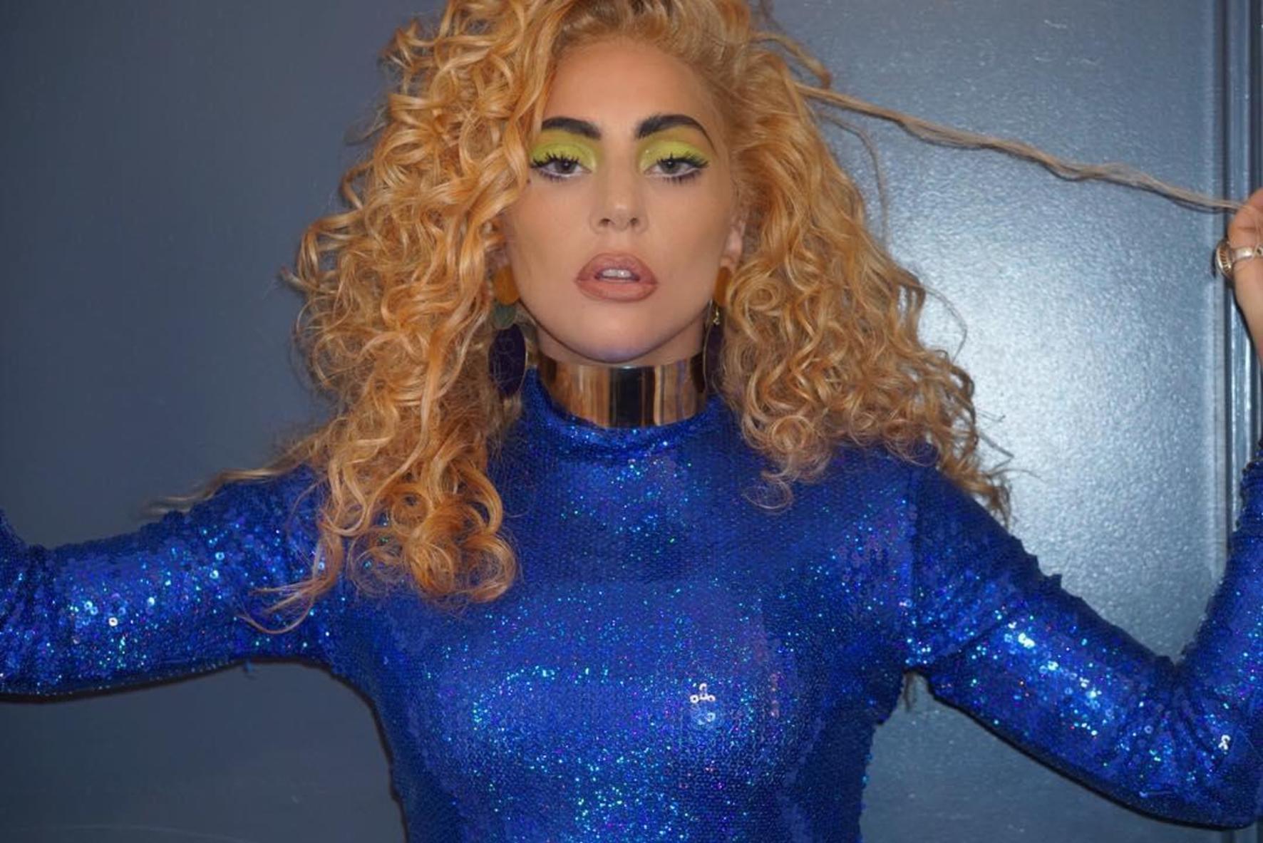 Lady Gaga, îmbrăcată într-un pulover albastru, cu părul creț, blond