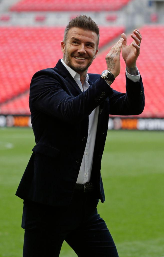 David Beckham într-un costum negru și cămașă albă, pe terenul de fotbal