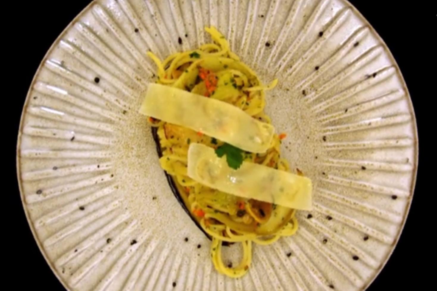Deasupra spaghetelor aglio olio cu peperoncino și vinete se așază felii subțiri de parmezan