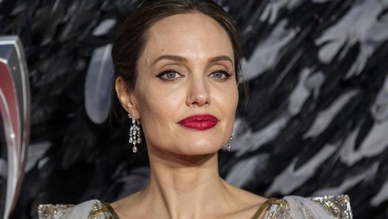 Angelina Jolie, îmbrăcată într-o rochie, cu ruj roșu pe buze, zâmbește