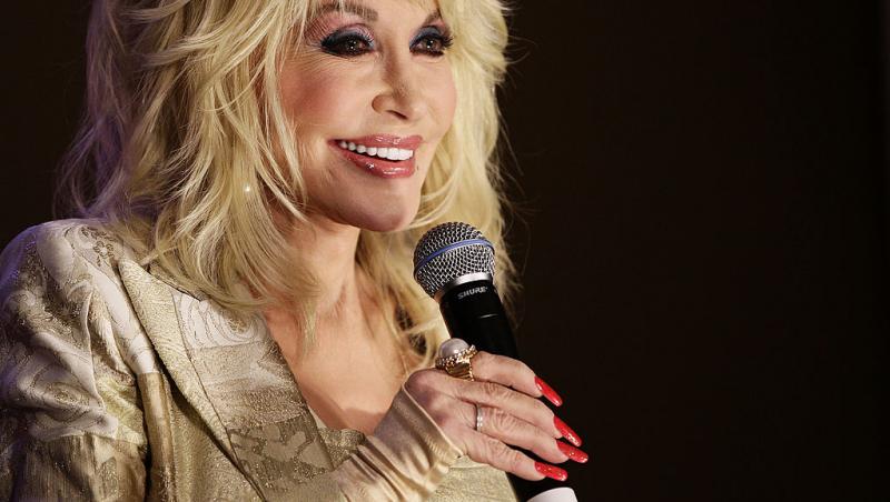 Dolly Parton, elegantă și frumos îmbrăcată, are un microfon în mână