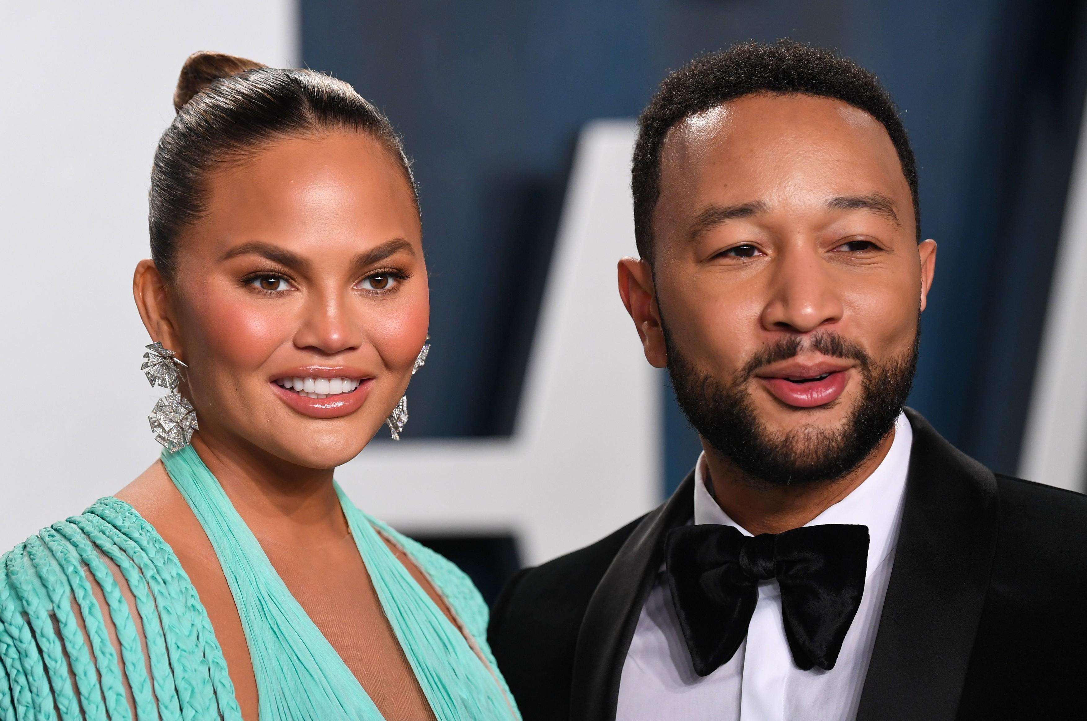 chrissy teigen, john legend, covor rosu, fundal alb cu albastru, rochie albastra, el in costum