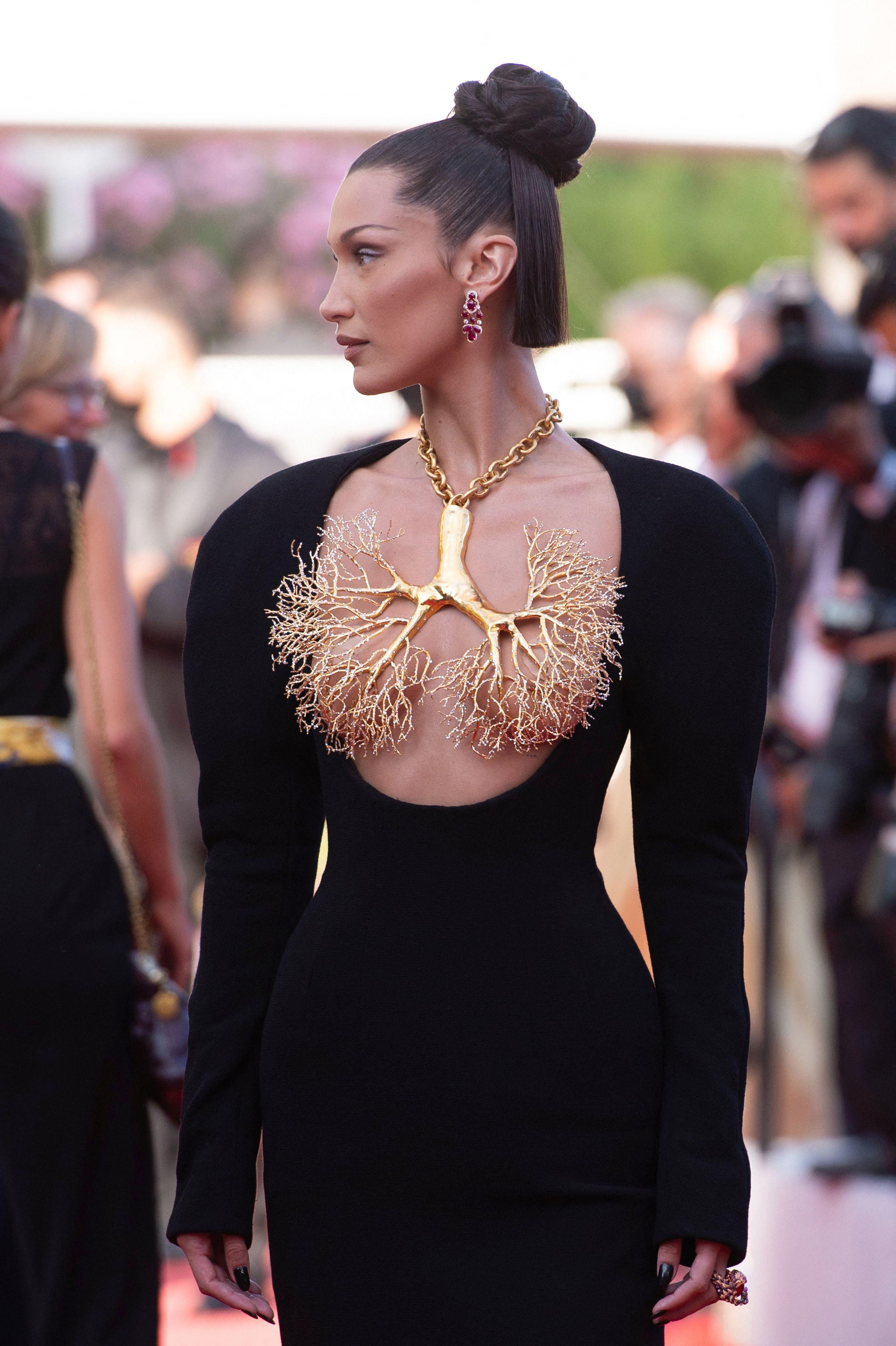 bella hadid intr-o rochie neagra, cu maneca lunga, parul prins in coc și un colier auriu in forma de plamani