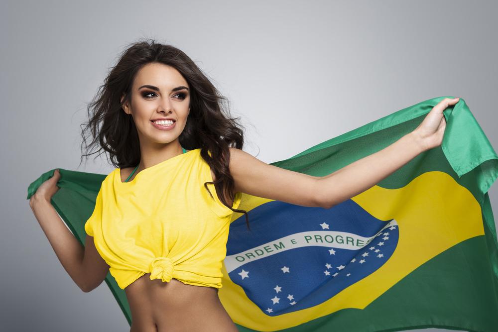 fata bruneta cu tricou galben tinand in spate steagul braziliei, zambind