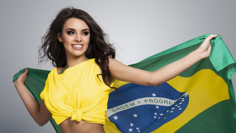 fata bruneta cu tricou galben tinand in spate steagul braziliei, zambind