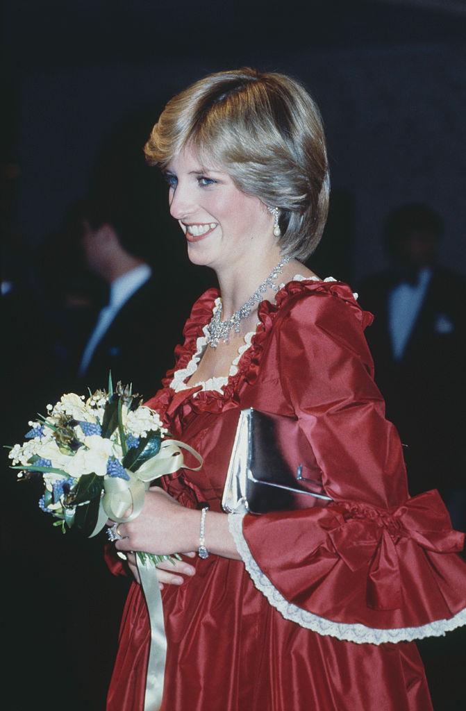 Prințesa Diana, într-o rochie roșie, ținând în mână un buchet de flori