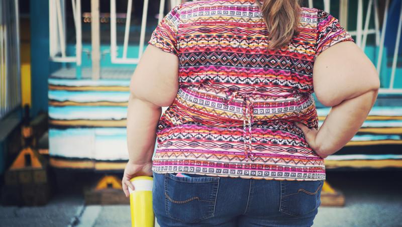 femeie supraponderala cu spatele, intr-o bluza cu imprimeu roz si jeansi