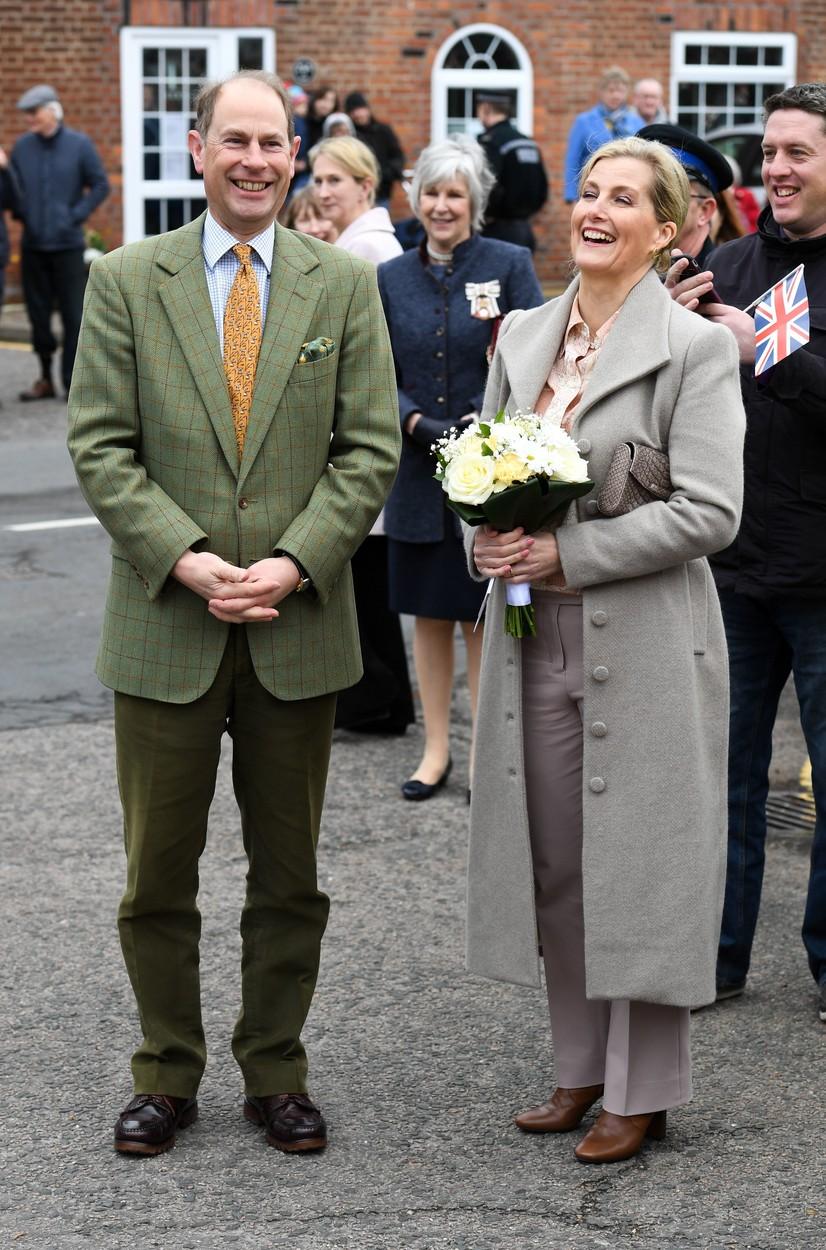 printul edward intr-un sacou verde si sotia lui sophie, avand un buchet de flori in mana, amandoi razand, in curtea castelului