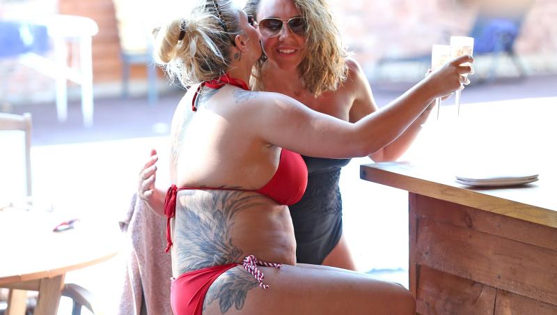 kerry katona in bikini roșu, strâmt, la bar cu o prietenă. părul blond prins sus, mobilă din lemn