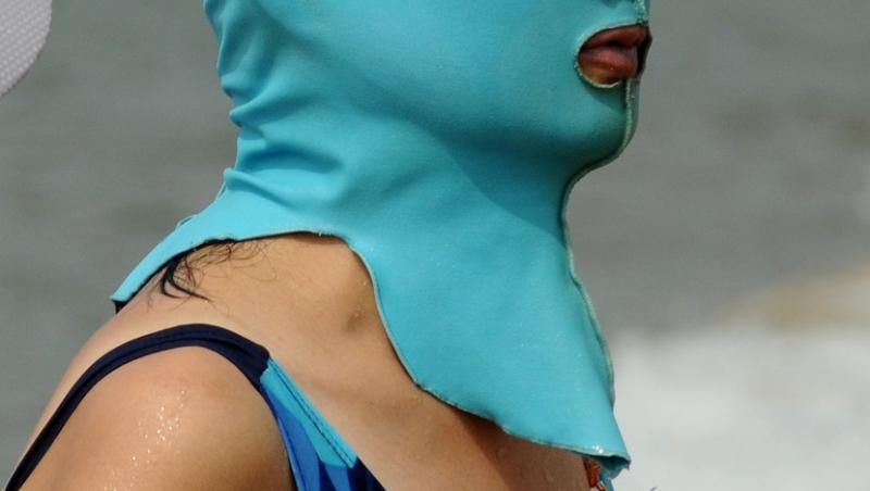 Femeie purtând o mască Facekini bleu, îmbrăcată în costum de baie
