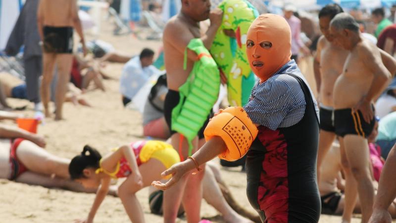 O persoană, pe plajă, purtând masca "Facekini"
