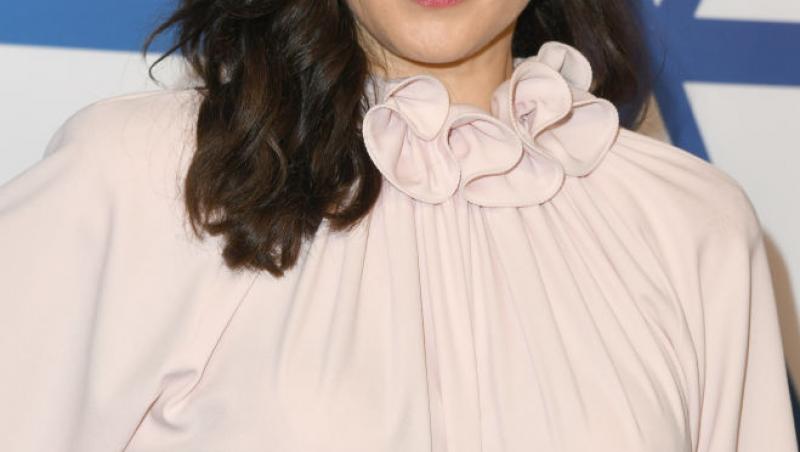Rachel Weisz, îmbrăcată într-o rochie crem, cu părul desprins și o mână în șold