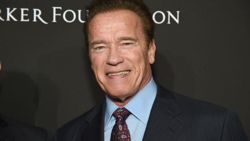 Arnold Schwarzenegger, la costum, zâmbește către camera foto