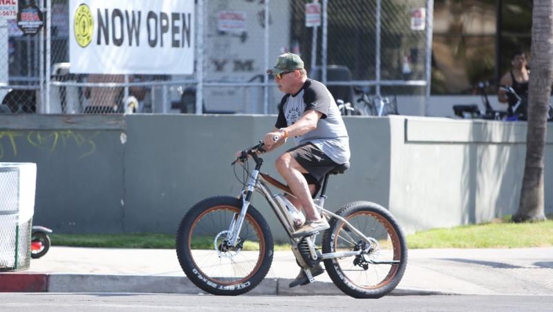 Schwarzenegger, pe bicicletă, purta o șapcă și ochelari de soare, pantaloni scurți și un tricou cu inscripția numelui unei săli de forță