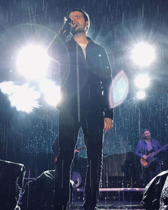 laurentiu duta imbracat in negru candtand pe scena, in ploaie