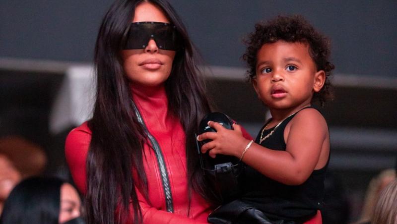 kim kardashian imbracata in rosu, cu ochelarii de soare negri la ochi, tinandul in brate pe fiul ei, la lansarea lui kanye west