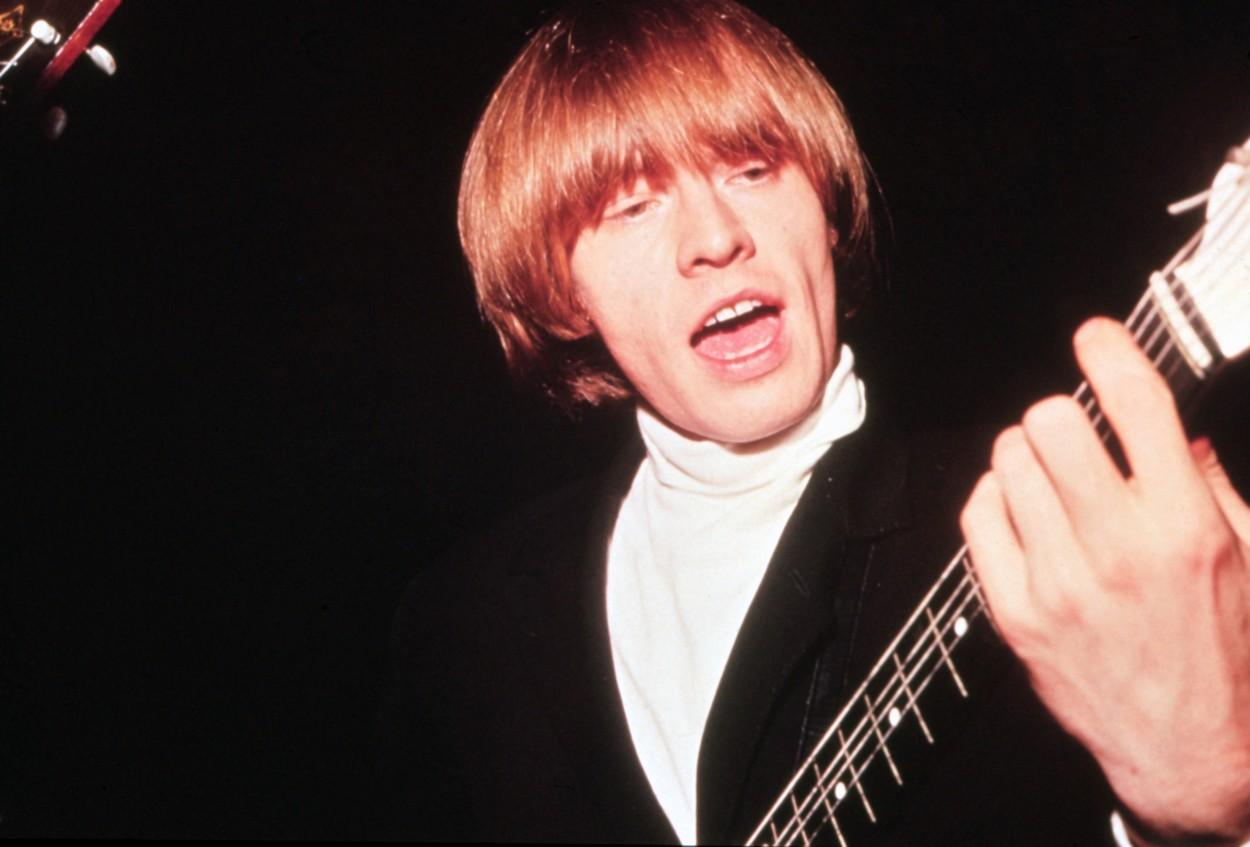 brian jones intr-o bluza alba, cu sacou negru si chitara in mana