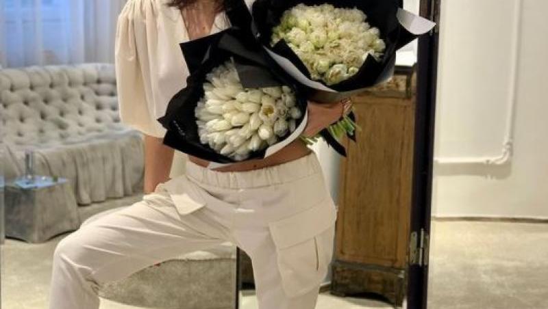 dana budeanu intr-un trening alb cu un buchet de flori albe in mana