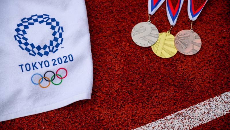trei medalii si un material alb pe care scrie tokyo 2020 cu simbolul jocurilor olimpice, pe un teren rosu