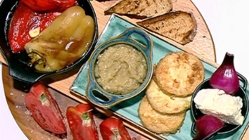 Salată de vinete cu dovlecei pane și salată de ardei copți, alături de roșii și brânză, pe un platou de lemn