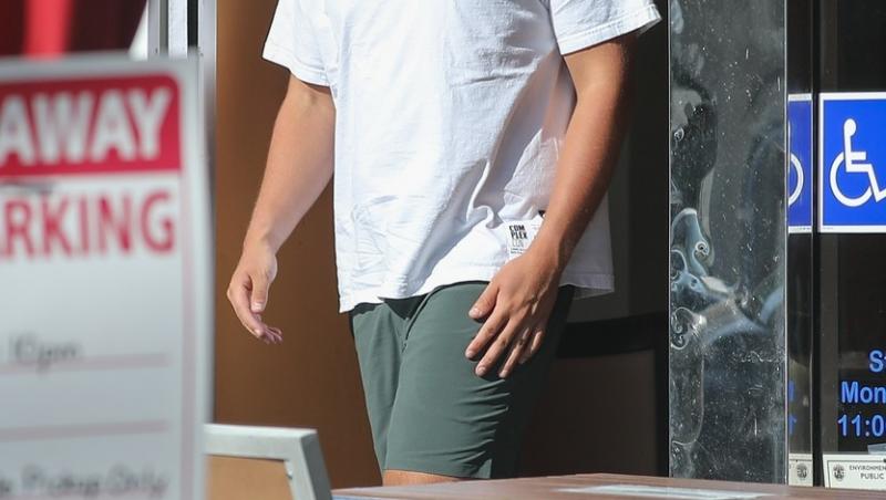 christopher schwarzenegger intr-un tricou alb si pantaloni verzi iesind dintr-un restaurant