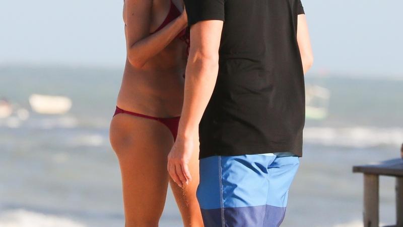 alessandra ambrosio și richard lee, la plajă în Brazilia, vara 2021. ea poartă un bikini roșu, el poartă un tricou negru și pantaloni scurți cu albastru și albastru închis. Fundal cu ocean și nisip