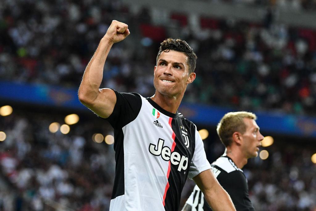 cristiano ronaldo pe terenul de fotbal intr-un tricou alb cu negru ridicand pumnul spre cer si muscandu-si buza