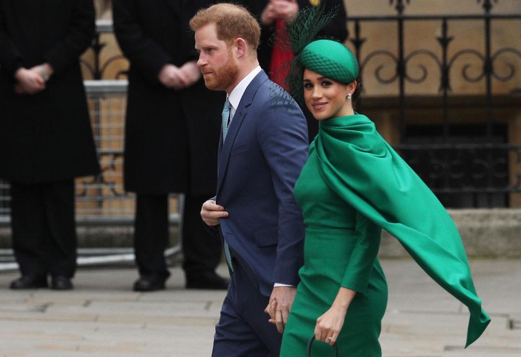 Meghan Markle, îmbrăcată într-o rochie verde, cu pălărie verde, și Prințul Harry, ținându-se de mână