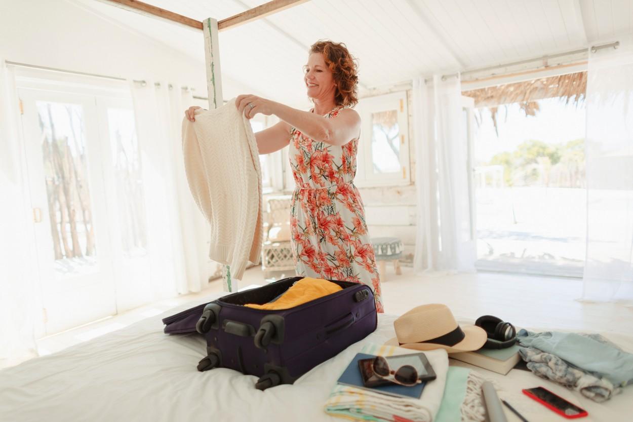 femeie care impacheteaza bagajul pe pat si pune haine in valiza pentru vacanta